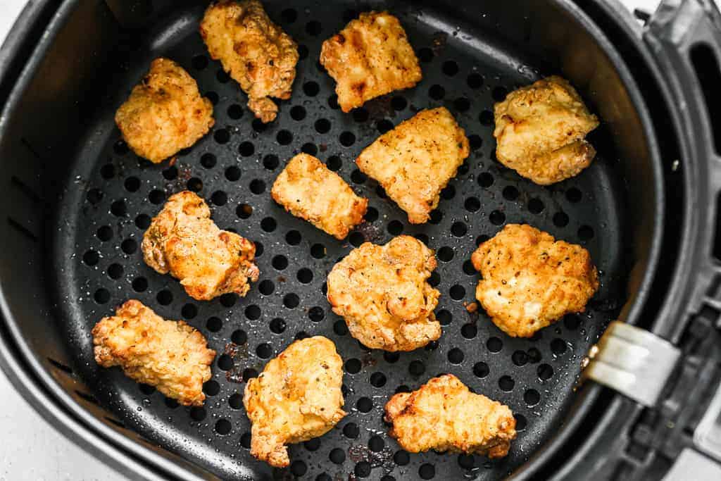 An air fryer basket with chicken nuggets inside.