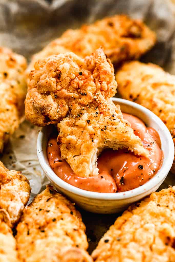 An Air Fried chicken tender being dipped in sauce.