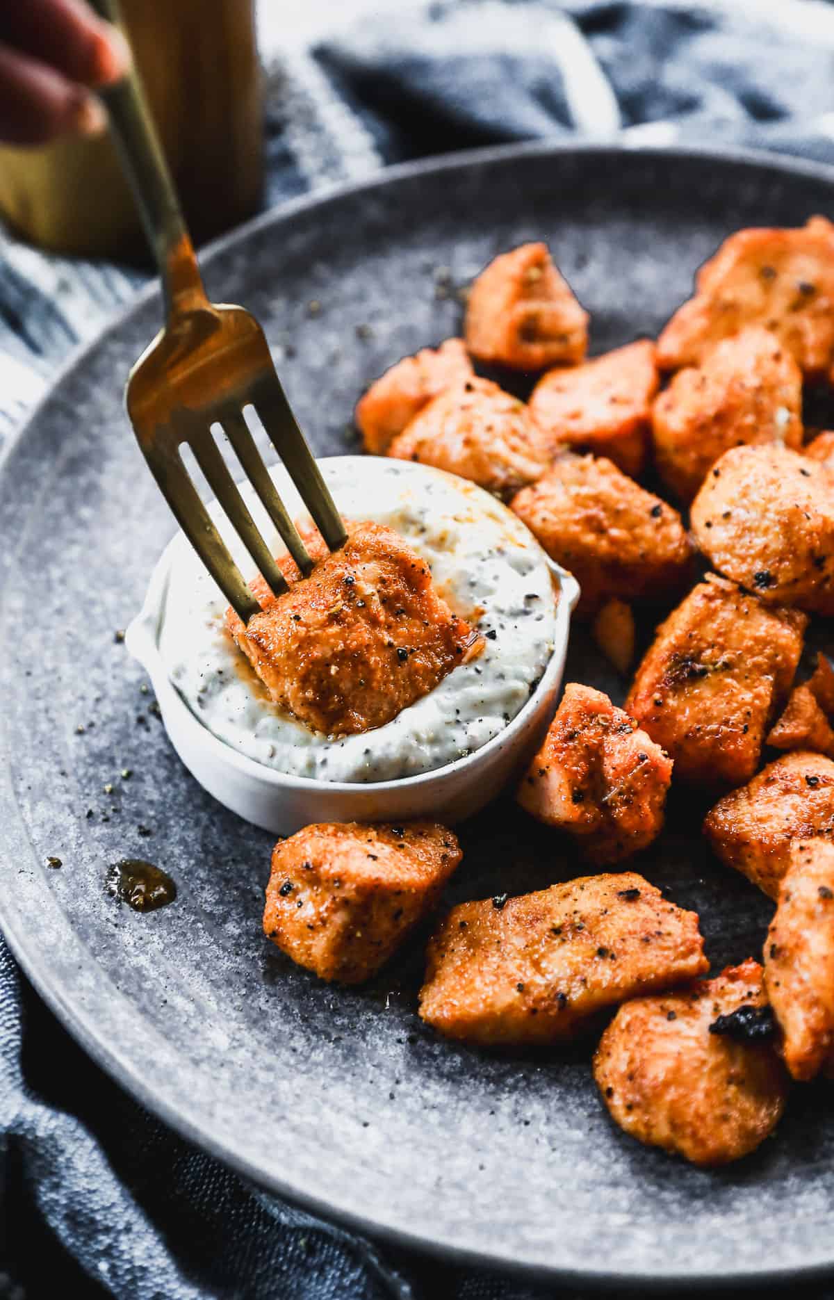 A fork holding a salmon bite and dipping it in remoulade sauce.