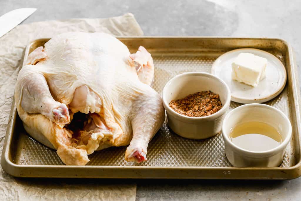 A whole chicken on a tray, with butter and seasonings to prepare air fryer whole chicken.