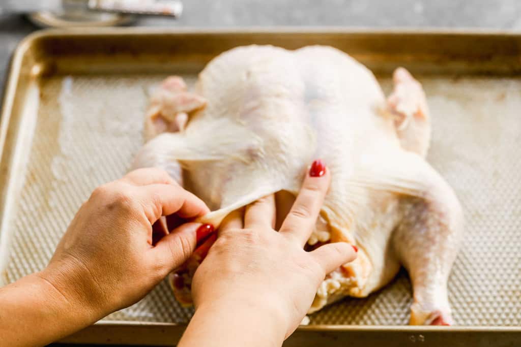 Butter being smoothed under the skin of a raw whole chicken.