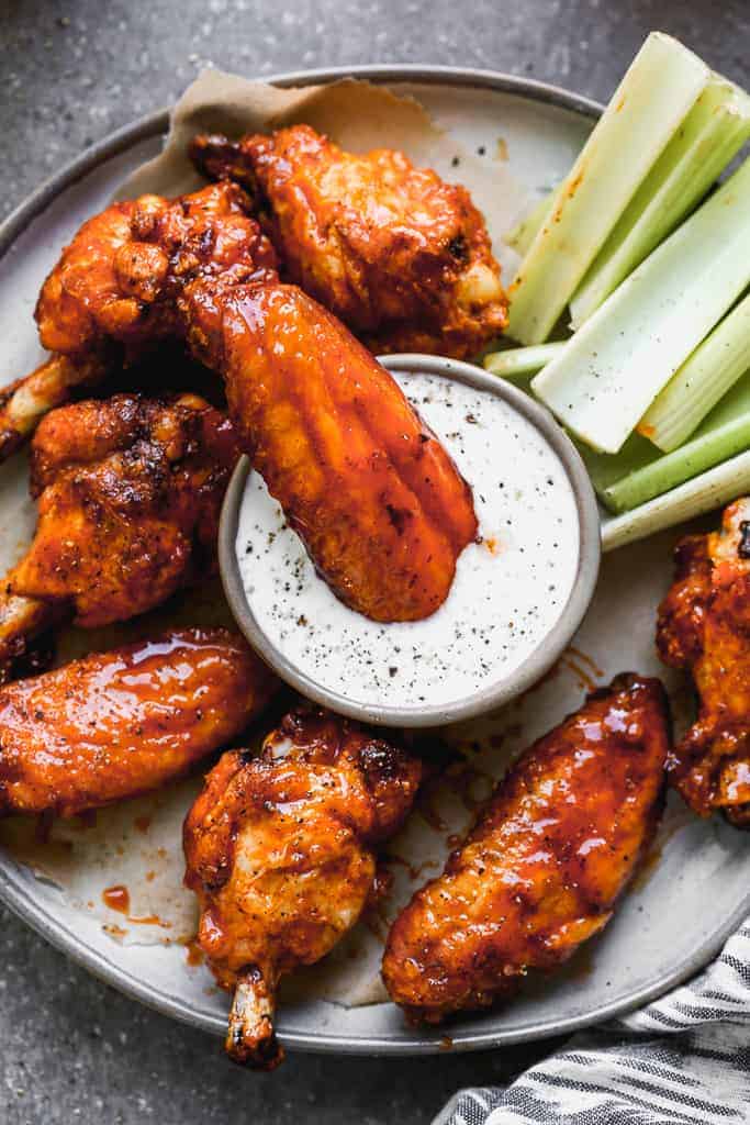 A plate with baked chicken wings and one wing dunking in ranch sauce.