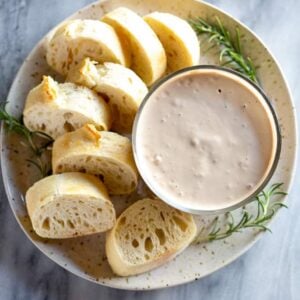 A bowl of balsamic bread dip on a plate with a sliced baguette.