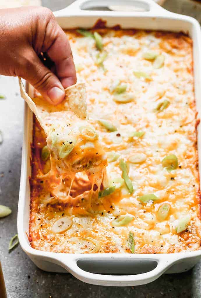 A pan of bean dip with a hand scooping a tortilla chip in it.