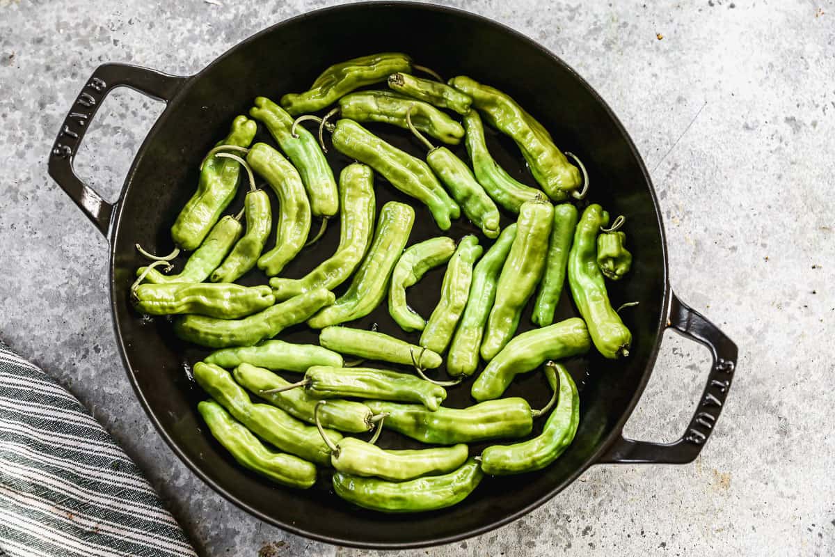 A cast iron pan with shishito peppers to make Blistered Shishito Peppers.