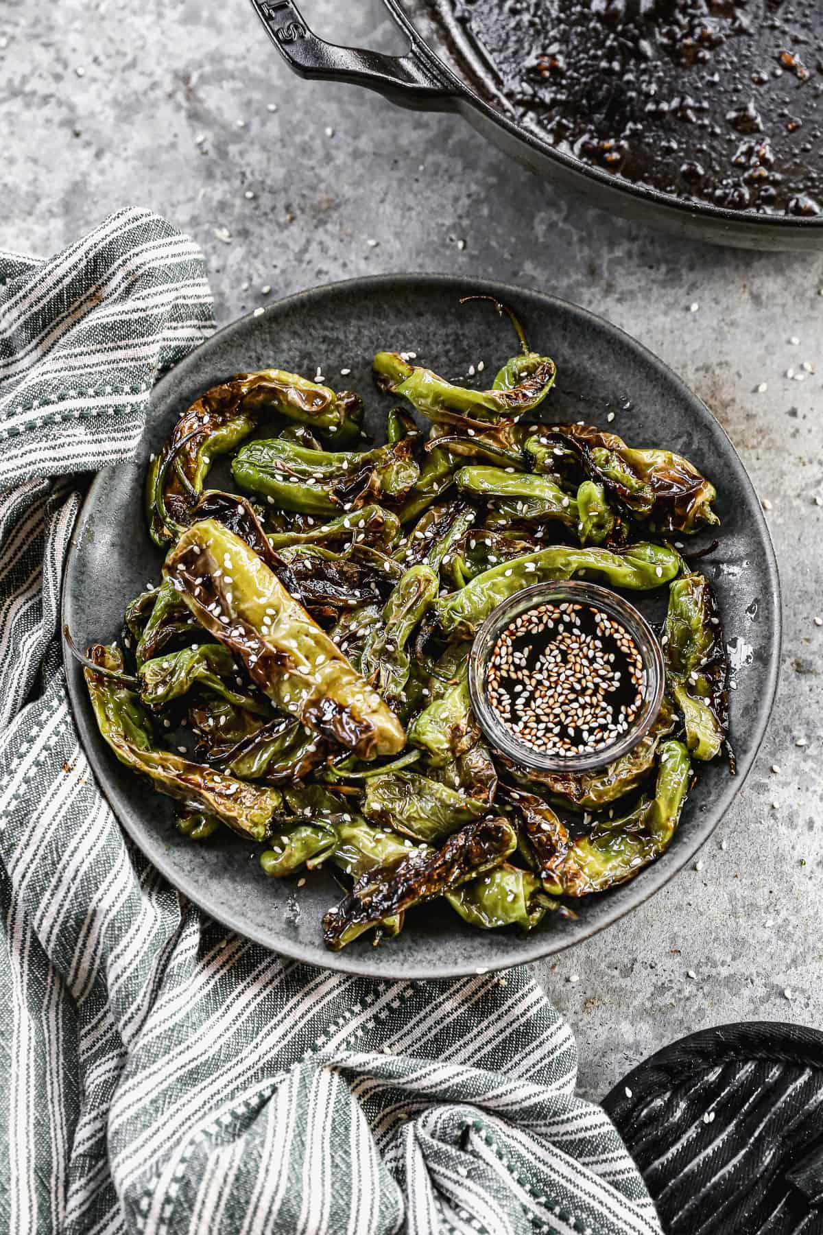 A plate full of easy Blistered Shishito Peppers, sprinkled with sesame seeds and served with a sesame dip. 