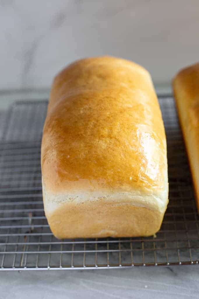 A loaf of homemade white bread cooling on a wire rack.