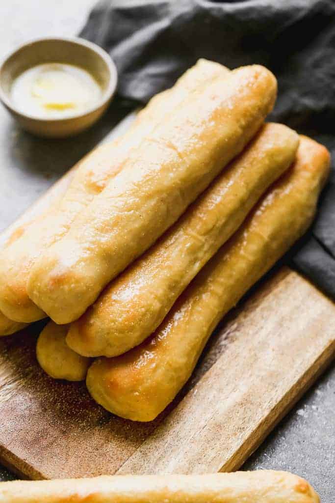 A stack of breadsticks with garlic butter on the side.