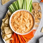 An easy Buffalo Chicken recipe in a white bowl surrounded by chips, celery, and carrots.