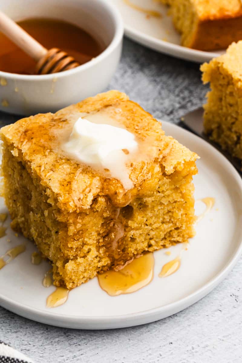 Moist buttermilk cornbread on a plate topped with butter and a drizzle of honey.