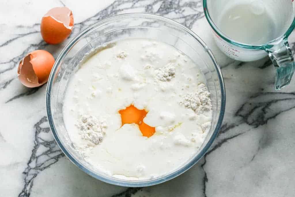 Buttermilk, eggs and melted butter added to a mixing bowl with dry pancake ingredients.