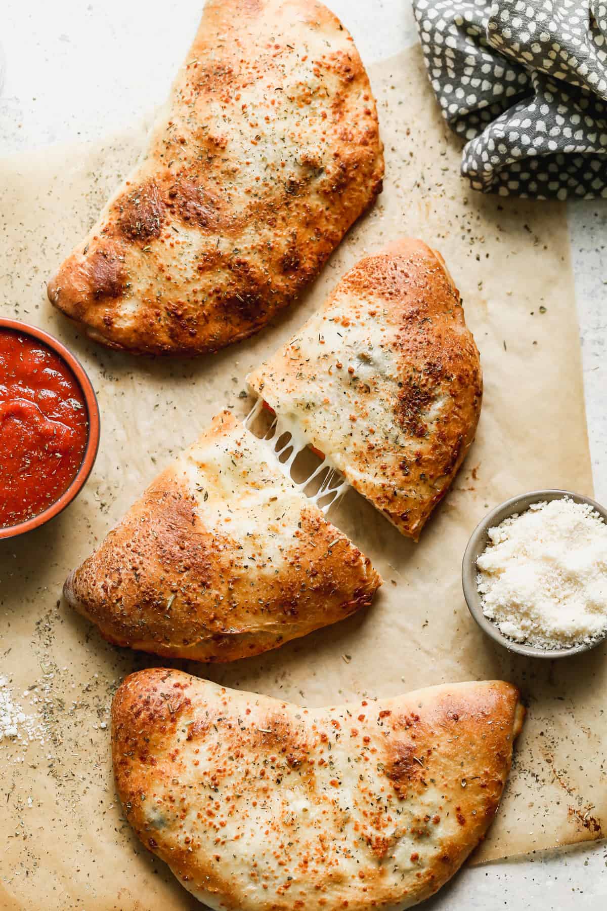 Three calzones on a piece of parchment paper with the middle one sliced in half.