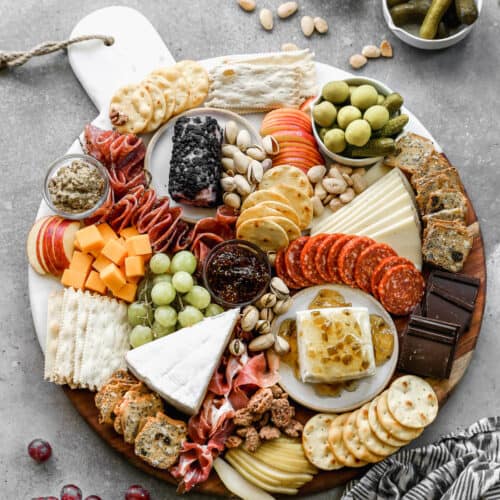 A large round charcuterie board with meats, cheese, fruits, nuts and crackers.