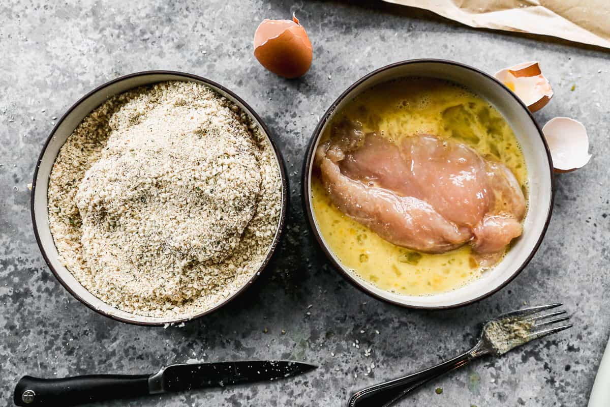 Two bowls showing the process of dipping and breading Chicken Parmesan. One bowl with chicken in an egg mixture, and the other one with chicken covered in a breading mixture.