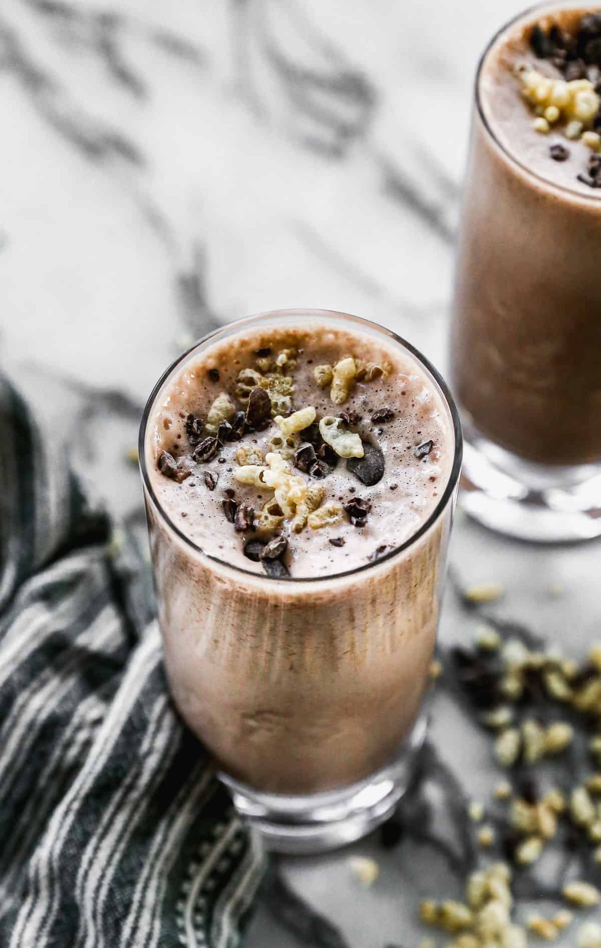 A close up image showing all the toppings on top of a chocolate protein shake, filled to the brim in a glass.