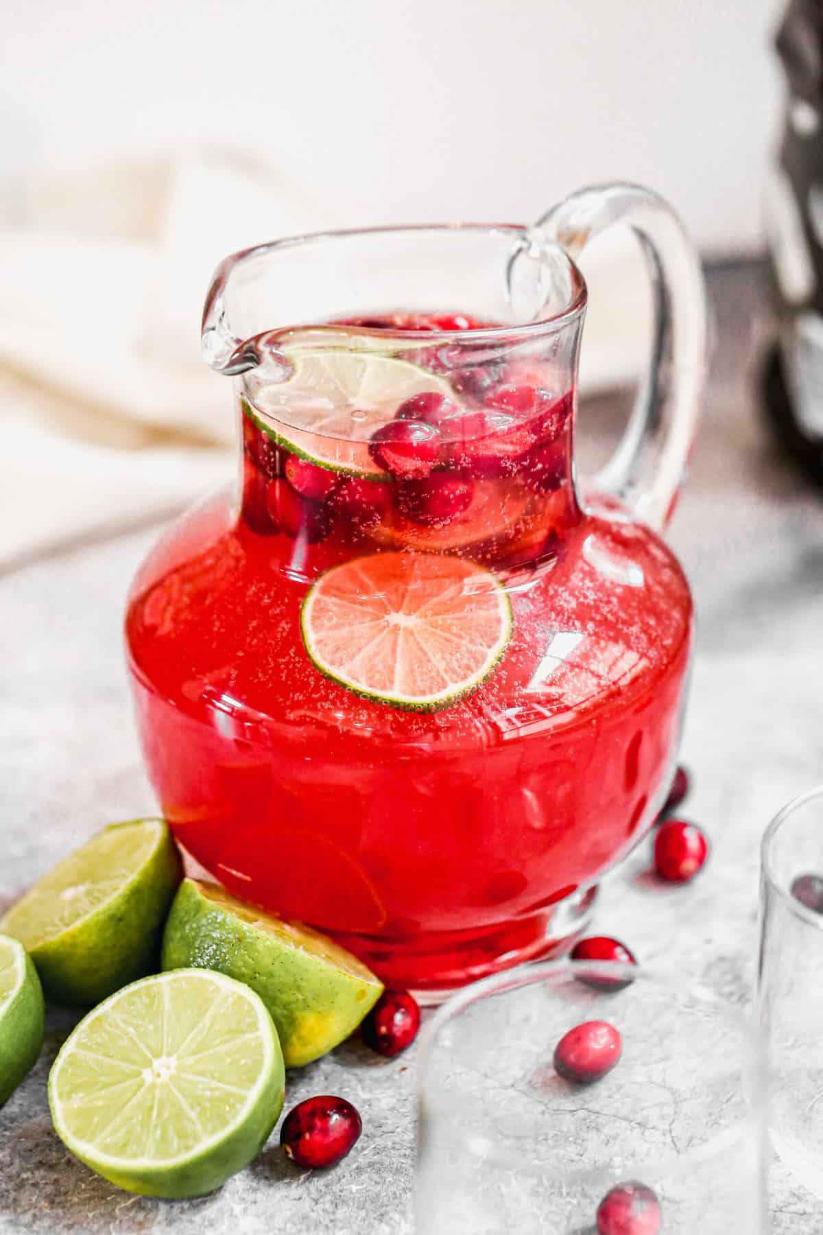 A large glass pitcher of homemade Christmas Punch with fresh cranberries and lime slices floating on top.