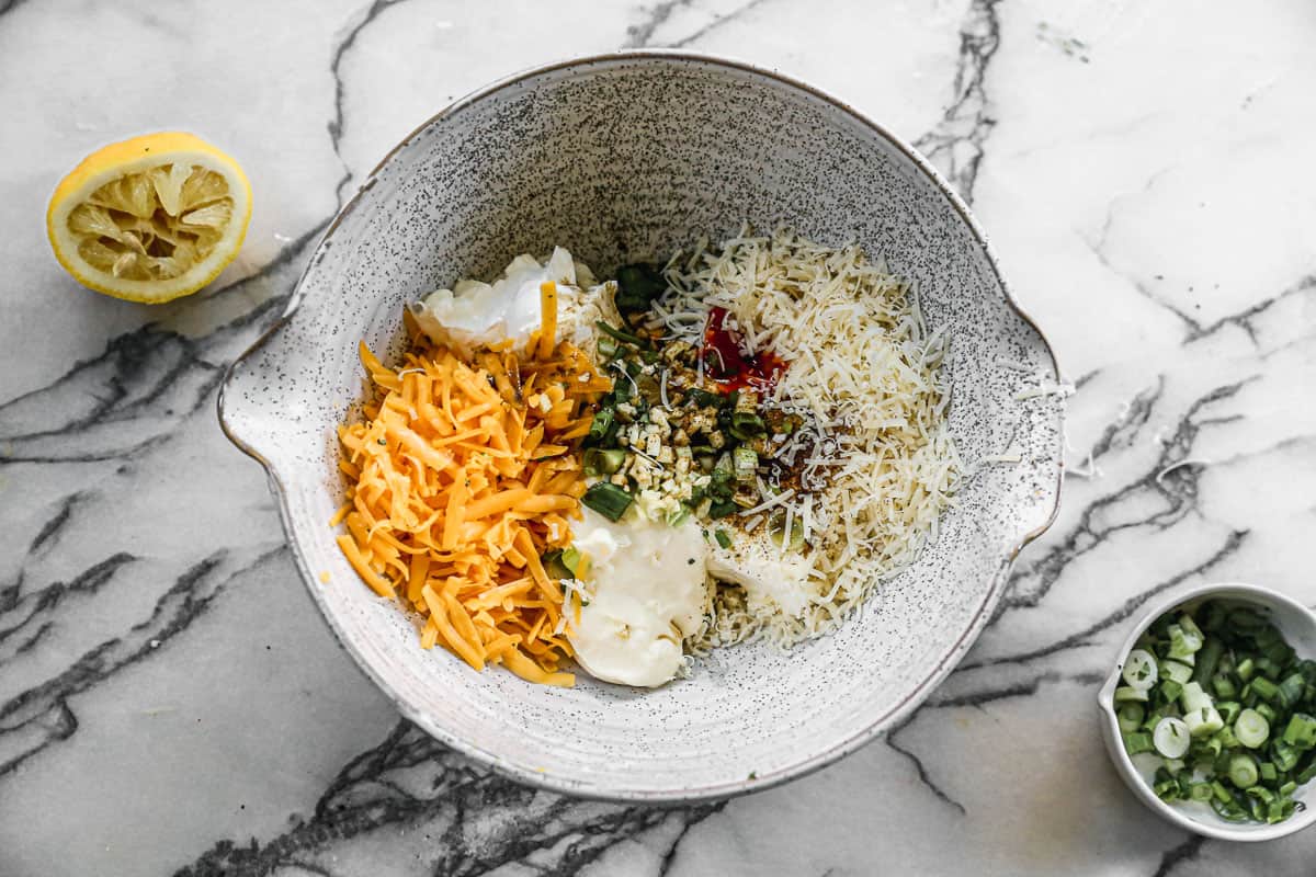 A mixing bowl filled with cream cheese, sour cream, mayo, garlic, green onion, old bay, lemon juice, cheese, and hot sauce to make an easy crab artichoke dip.