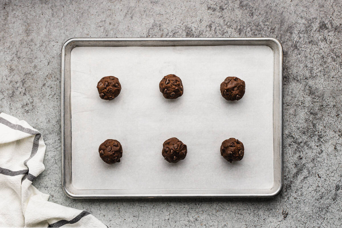 Six large chewy double chocolate chip cookies on a baking sheet with parchment paper, ready to be baked.