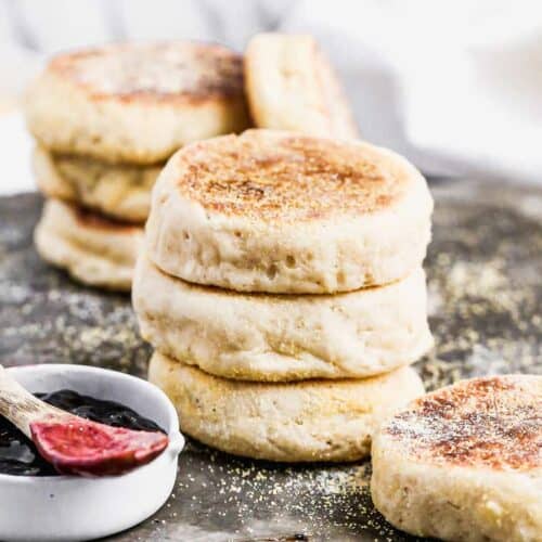 Three homemade English Muffins stacked on each other on a baking sheet.