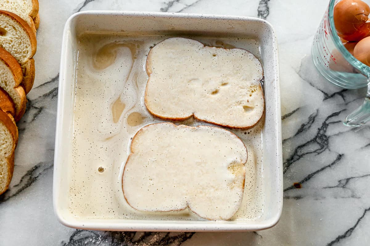 Two slices of bread being dipped into a batter.