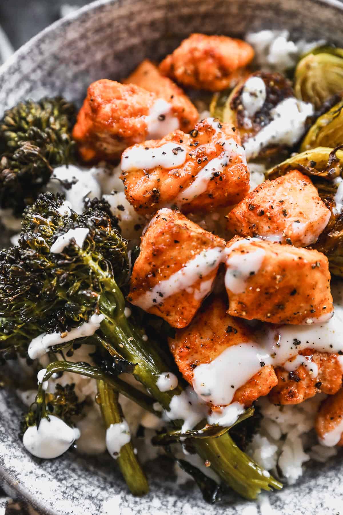 A close up image of a spicy salmon bowl recipe, drizzled with ranch and hot honey. 