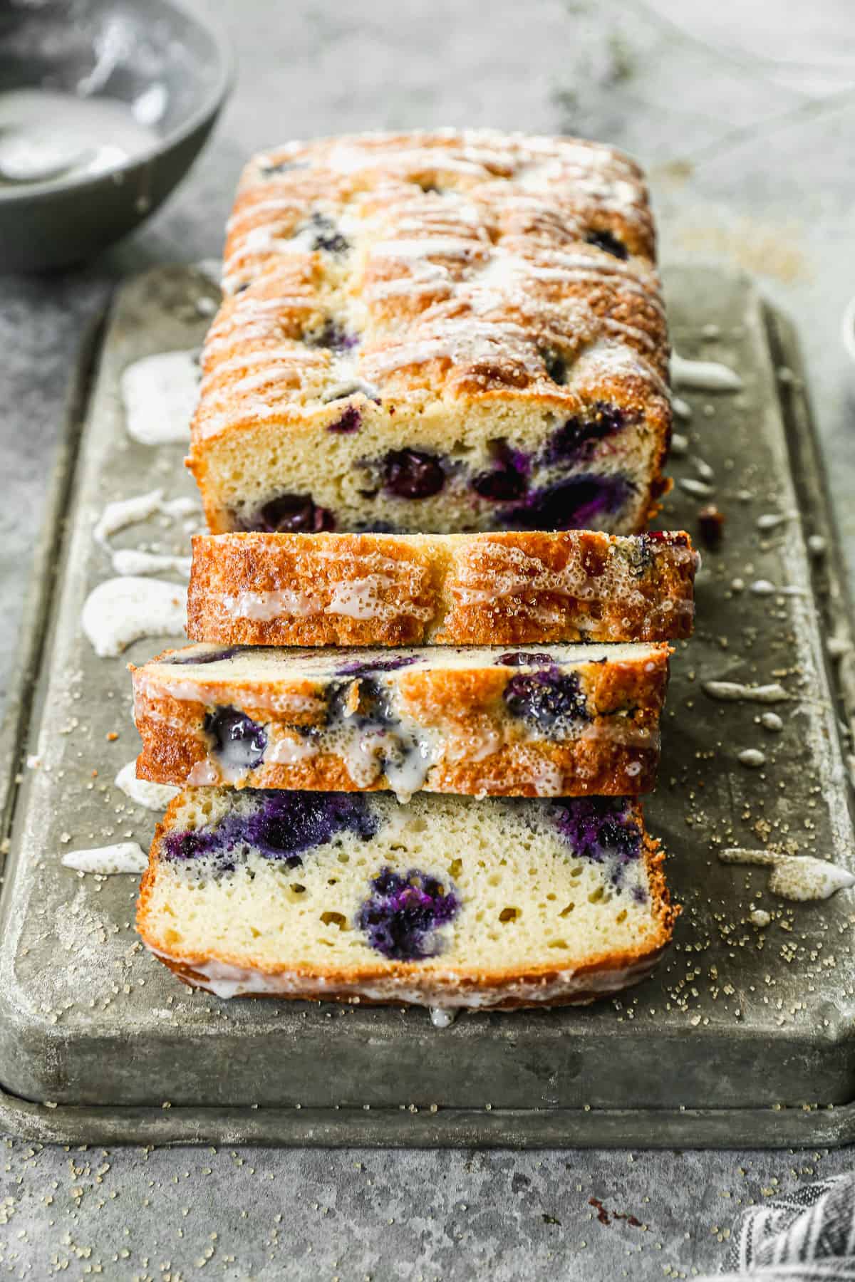 A loaf of Lemon Blueberry Bread with half of it sliced and ready to eat.