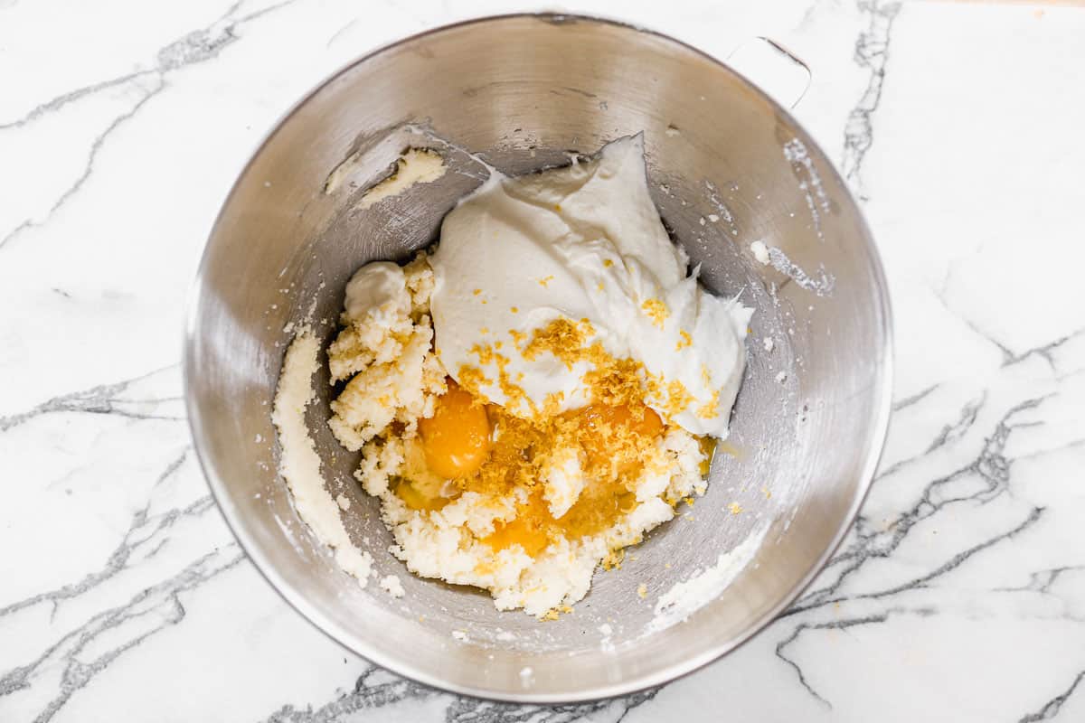 A metal mixing bowl with sugar, oil, butter, yogurt, eggs, lemon zest, and vanilla for moist lemon poppy seed bread.