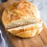 No Knead Bread on a wood cutting board with two slices cut from it and a butter tray in the background.