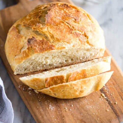 No Knead Bread on a wood cutting board with two slices cut from it and a butter tray in the background.