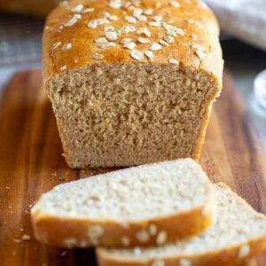 Oatmeal bread on a bread board with two slices cut from it.