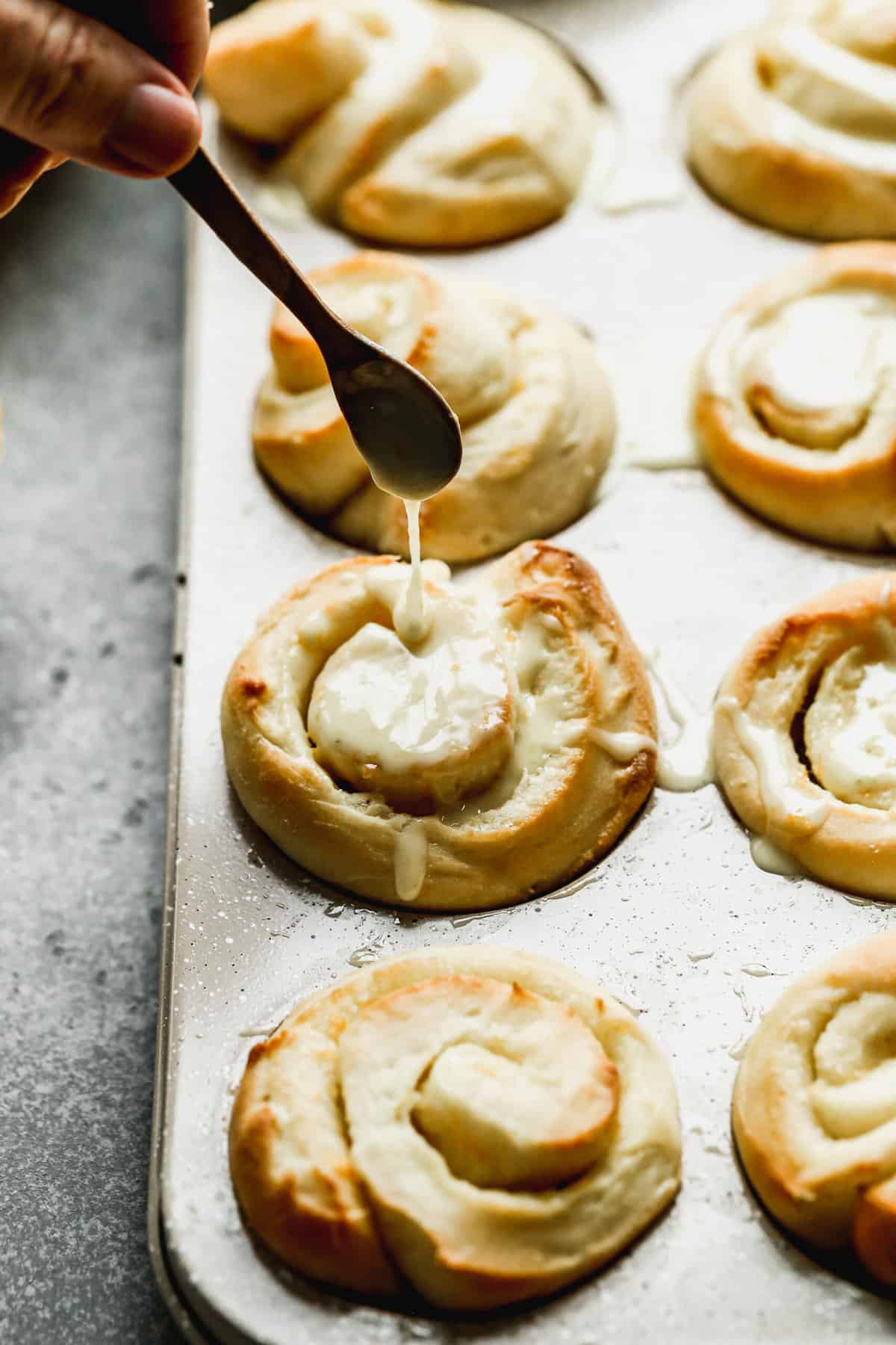 Homemade orange glaze being drizzled on top of the best orange rolls, warm from the oven.