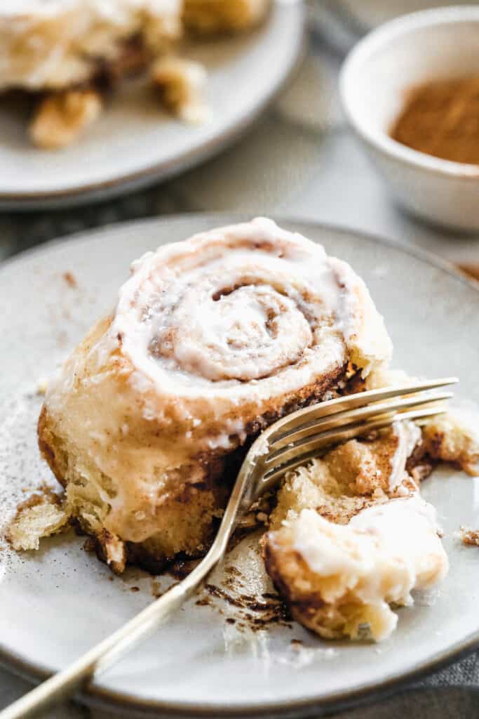 A cinnamon roll frosted with cream cheese frosting, on a plate with a fork.