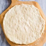 Pizza dough stretched into a round circle and pricked with a fork on a wooden pizza peel.