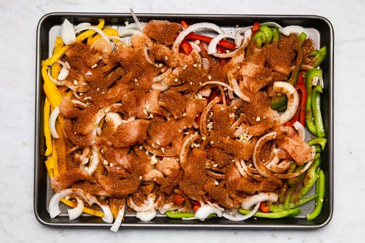 Fajita seasoning sprinkled over sliced chicken and vegetables on a pan.