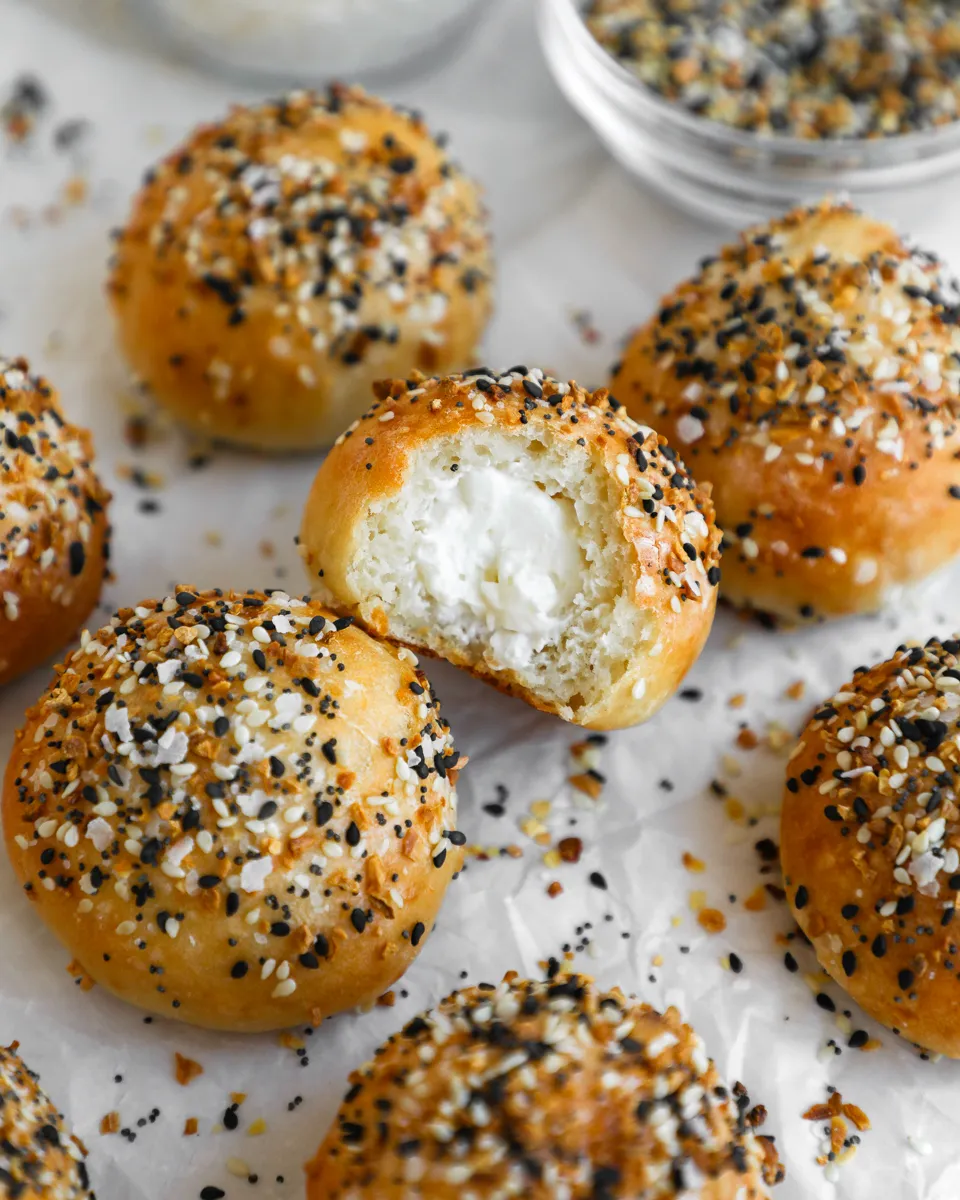 Everything Bagel balls filled with cream cheese, one with a bite taken out of it to show the inside.