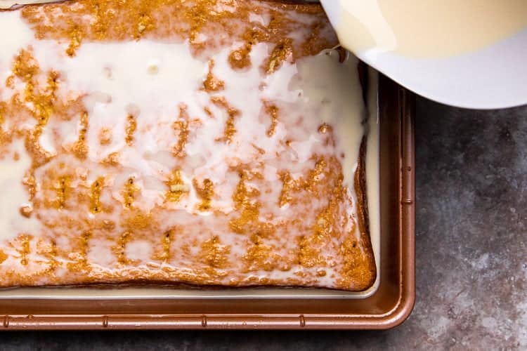 Milk mixture being poured over a cake in a pan, with holes poked in the cake.