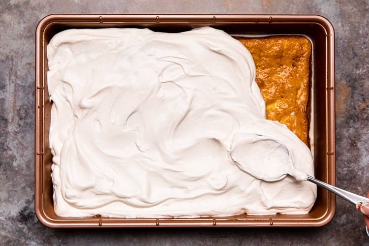 Whipped cream being spread over the top of a cake.