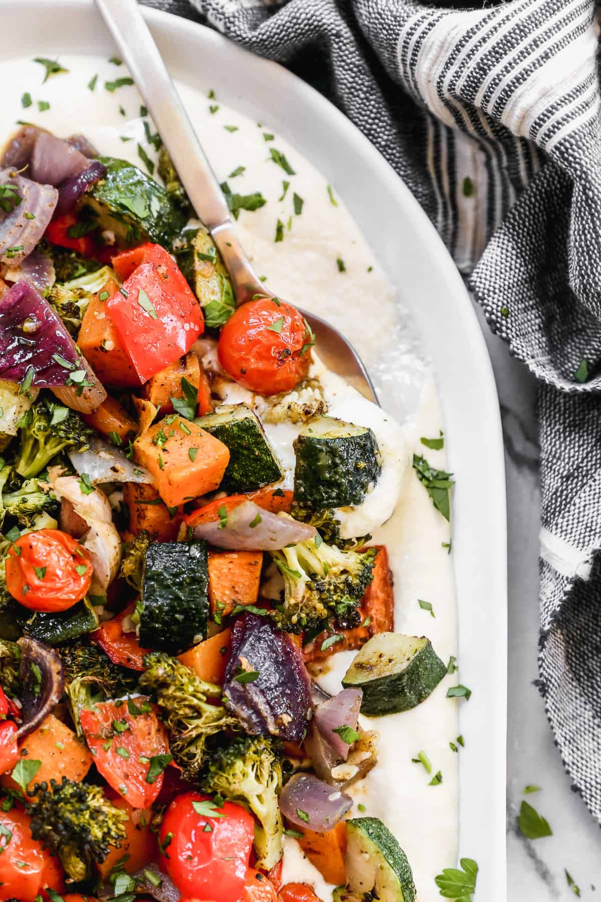 A close image of whipped feta dip with roasted vegetables and herbs with a spoon scooping some.