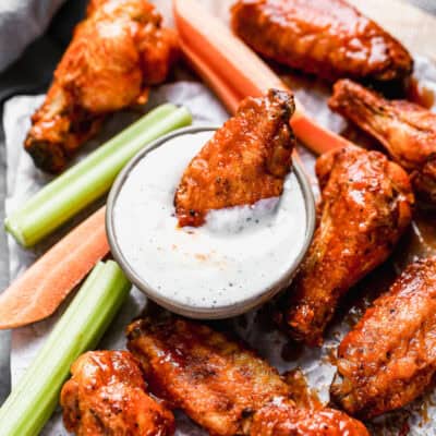 A crispy Air Fryer Chicken Wings recipe tossed in a simple buffalo sauce, being dipped in a cup of ranch.