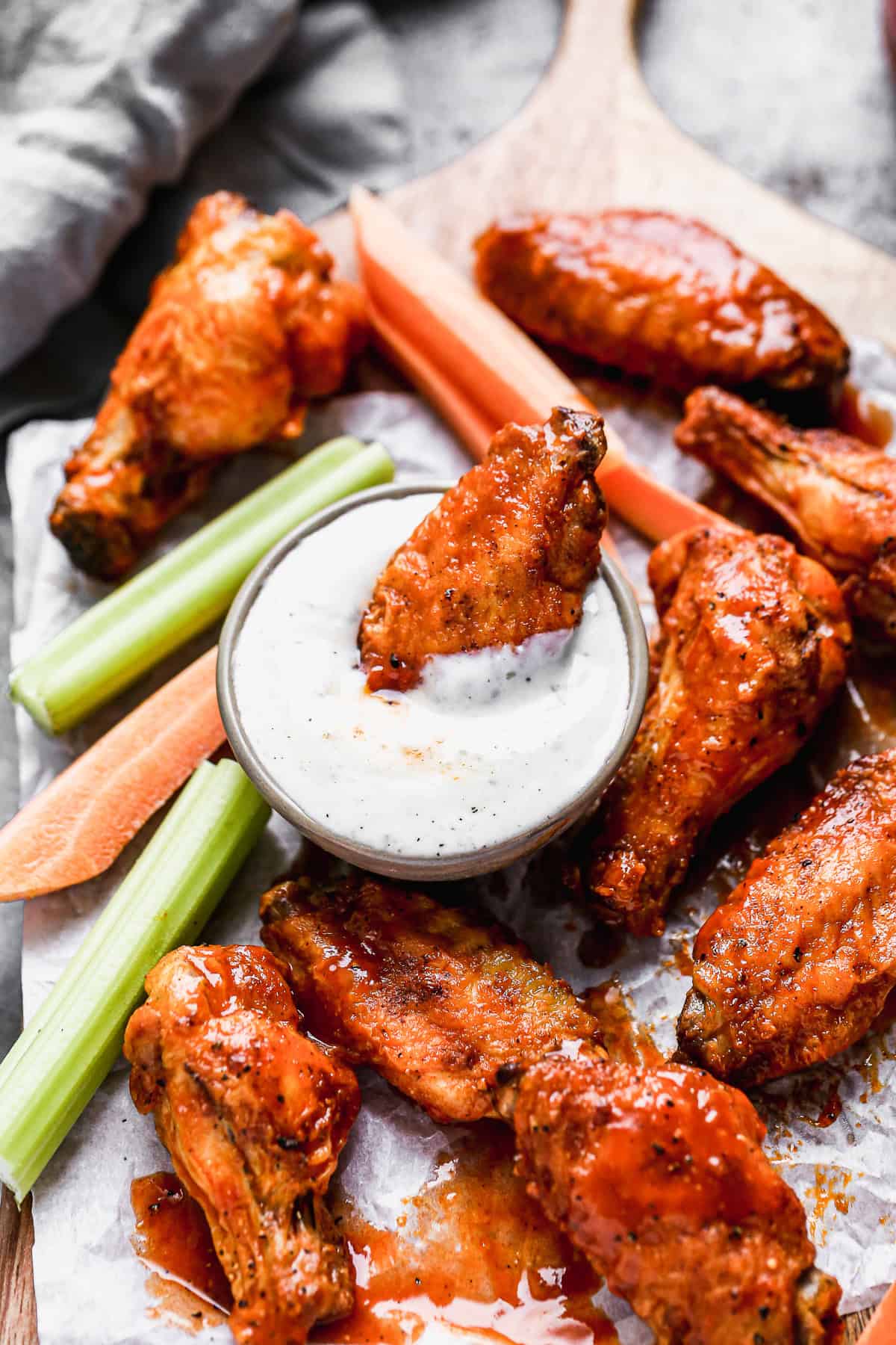 A crispy Air Fryer Chicken Wings recipe tossed in a simple buffalo sauce, being dipped in a cup of ranch.