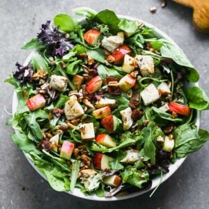 Overhead view of a green salad with grilled, chopped chicken, chopped apples, bacon and pecans.