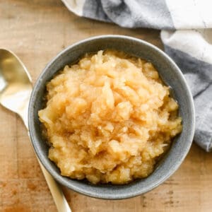 A bowl of homemade applesauce, next to a spoon.