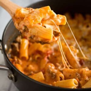 Baked Ziti made in a skillet with ziti noodles, cheese and sausage, with a wooden spoon scooping out a serving.