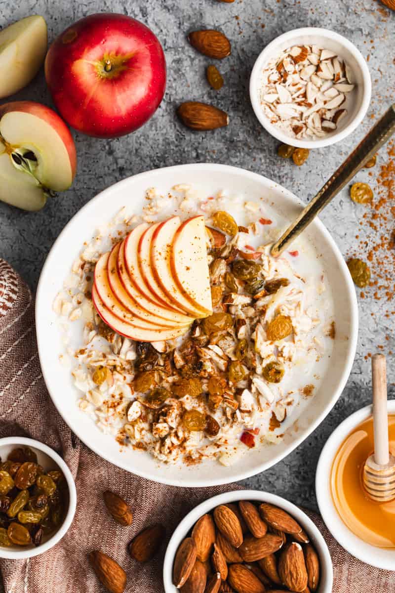 A bowl of a Swiss Bircher Muesli recipe packed with grated apple, golden raisins, almonds, honey, and a sprinkle of cinnamon. 