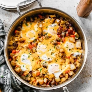 An easy Breakfast Skillet recipe in a large stainless steel pan with potatoes, eggs, bacon, sausage, and shredded cheese.