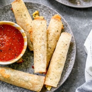 Five breakfast taquitos on a plate with a small bowl of salsa.