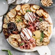 An easy Burrata appetizer drizzled with a balsamic reduction and arranged on a platter with mini toasts, jam, prosciutto, fresh pear, and dates.