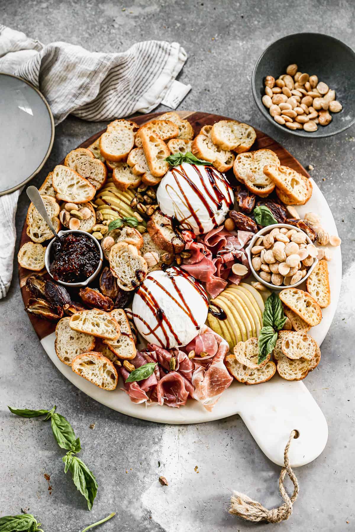 An easy Burrata appetizer drizzled with a balsamic reduction and arranged on a platter with mini toasts, jam, prosciutto, fresh pear, and dates. 