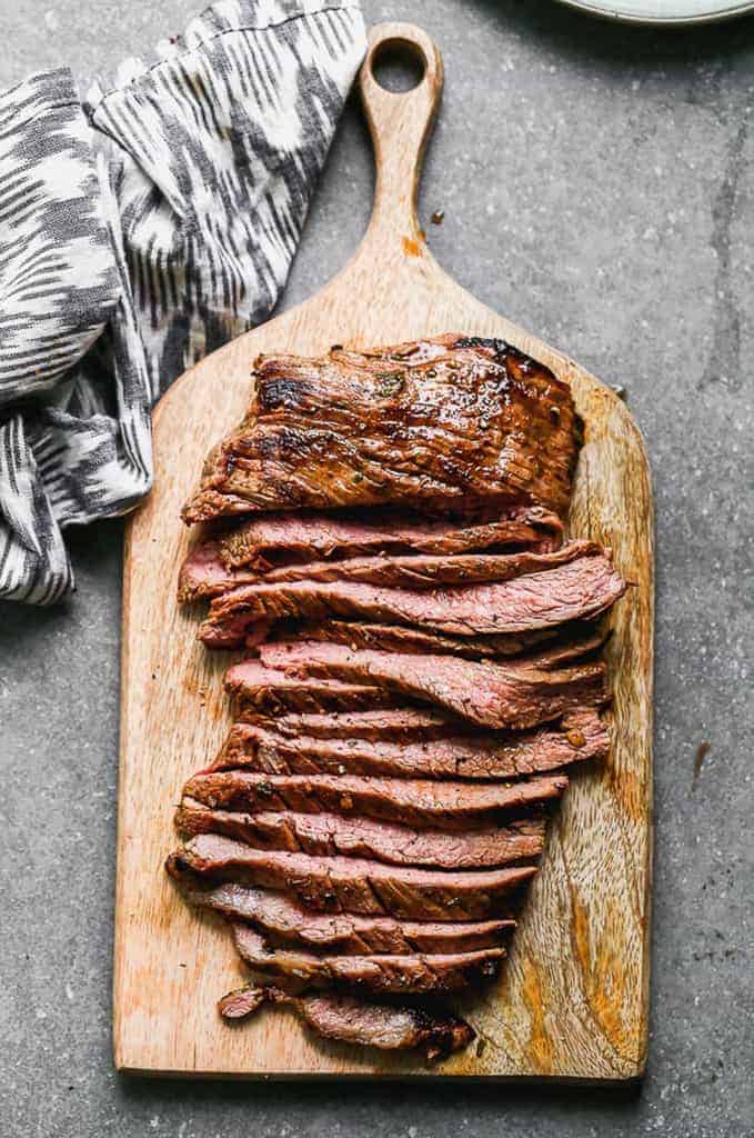 Grilled, sliced carne asada steak, served a on wooden board.