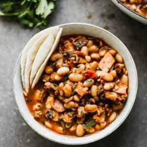 Charro beans served in a bowl with tortillas on the side.